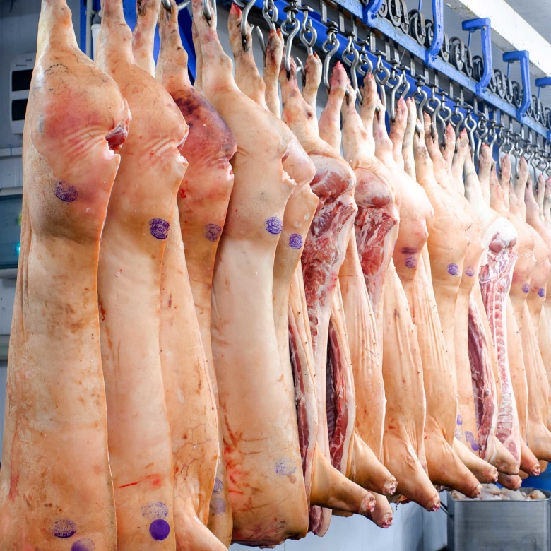 Schweinehälften hängen in Reihe am Haken