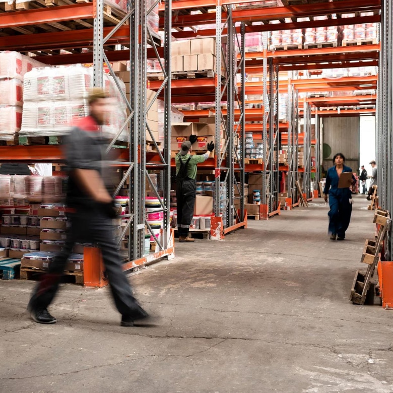 Menschen laufen geschäftig in einem Lager mit Hochregalen.
