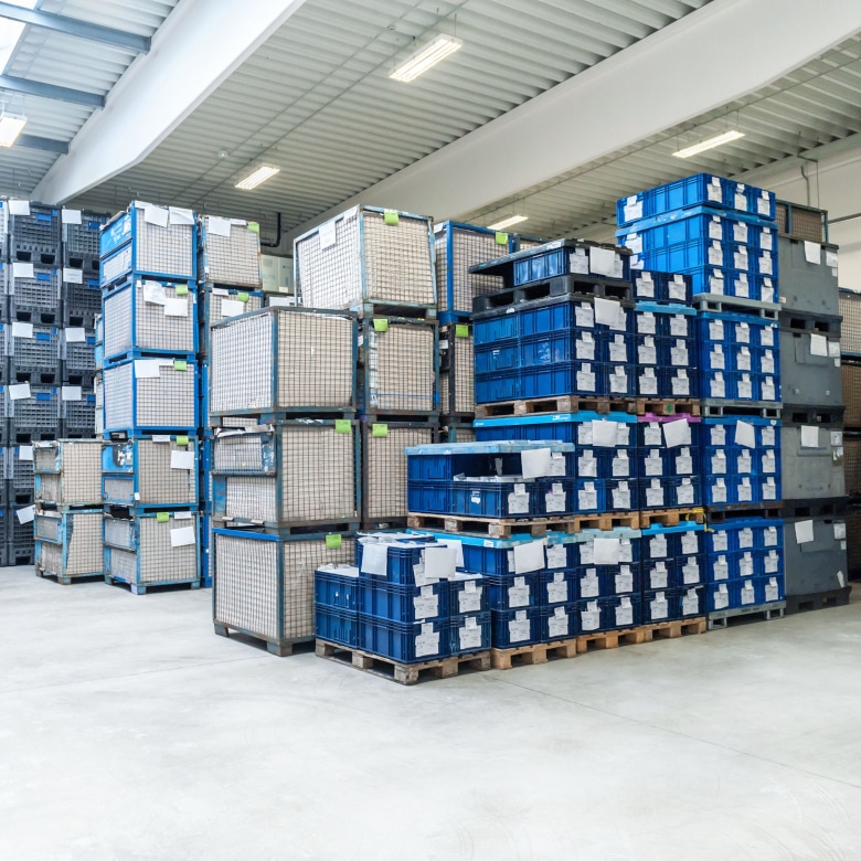 Lager mit hoch gestapelten Paletten, darauf blaue Kisten.